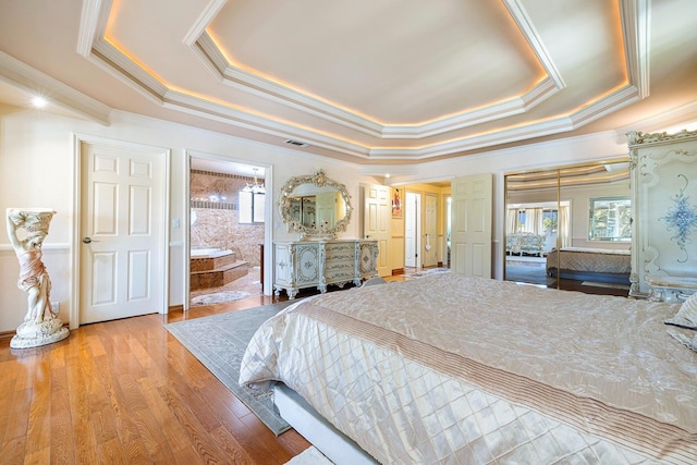 bedroom with crown molding, connected bathroom, a tray ceiling, and light hardwood / wood-style floors