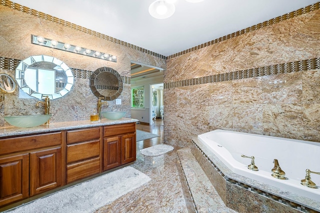 bathroom with a relaxing tiled tub, vanity, and tile walls