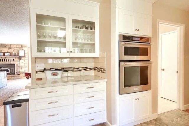 kitchen featuring a fireplace, stainless steel double oven, a textured ceiling, and white cabinetry