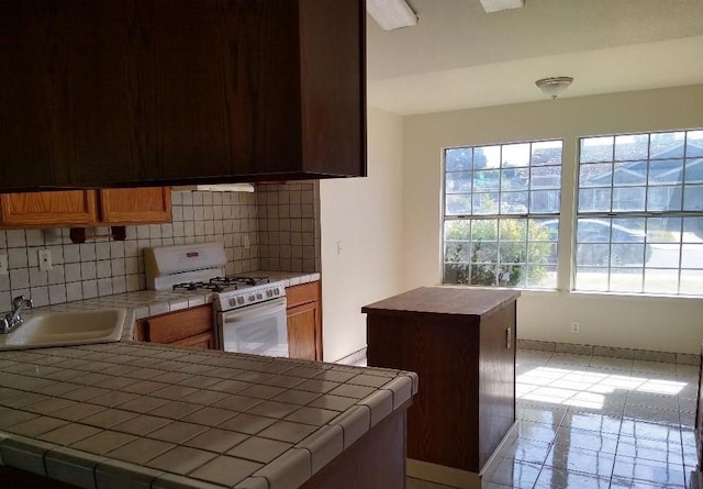 kitchen featuring tasteful backsplash, tile counters, sink, and white gas range