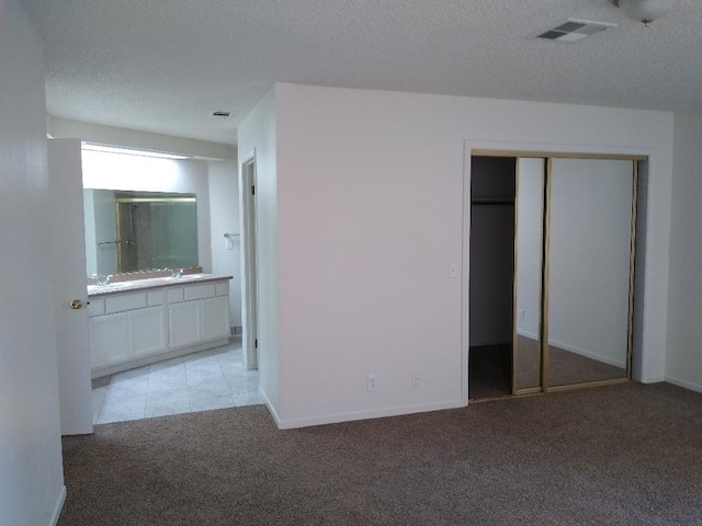 unfurnished bedroom with sink, a textured ceiling, light carpet, and a closet