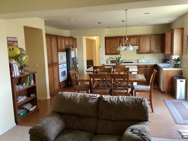 interior space with pendant lighting, white appliances, sink, light wood-type flooring, and a chandelier