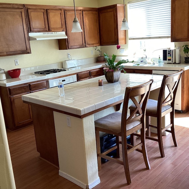 kitchen with pendant lighting, light hardwood / wood-style flooring, tile counters, a kitchen island, and a breakfast bar area