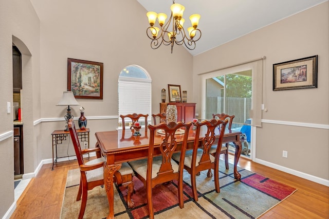 dining area with light wood-type flooring, high vaulted ceiling, and an inviting chandelier