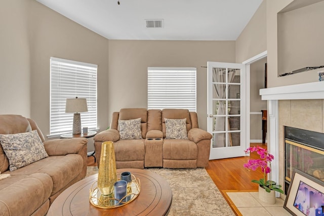 living room featuring a tiled fireplace, light hardwood / wood-style flooring, and a healthy amount of sunlight