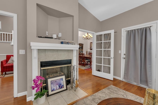 living room featuring a tiled fireplace, high vaulted ceiling, a chandelier, and light hardwood / wood-style floors