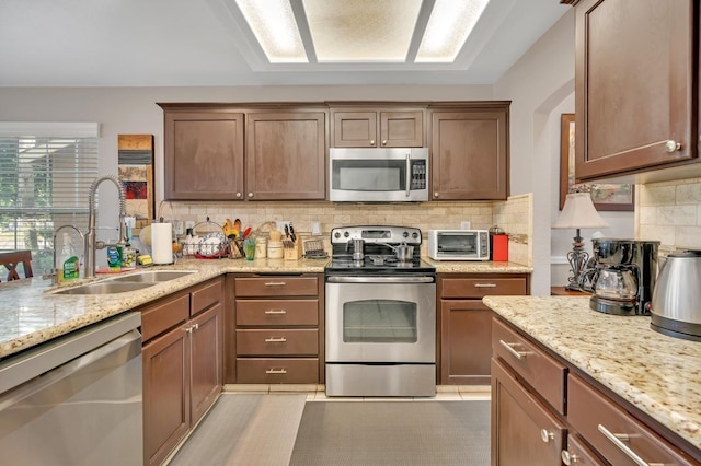 kitchen with stainless steel appliances, light tile patterned floors, decorative backsplash, light stone countertops, and sink