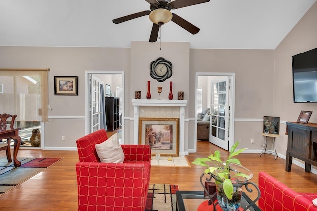 living room with ceiling fan, a tile fireplace, vaulted ceiling, and wood-type flooring