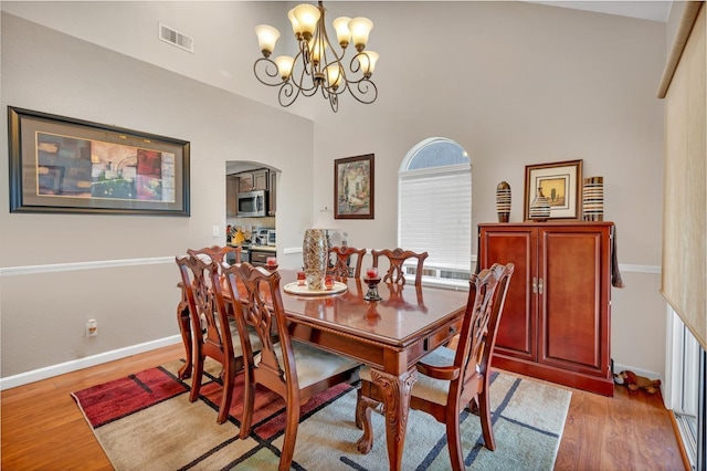 dining area with a towering ceiling, wood-type flooring, and an inviting chandelier