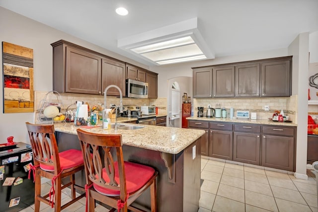 kitchen featuring appliances with stainless steel finishes, light stone countertops, backsplash, light tile patterned floors, and kitchen peninsula