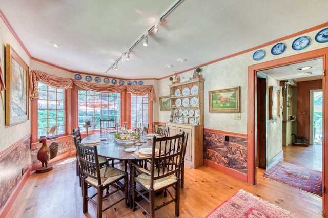 dining area featuring wallpapered walls, light wood-style flooring, a wainscoted wall, and ornamental molding