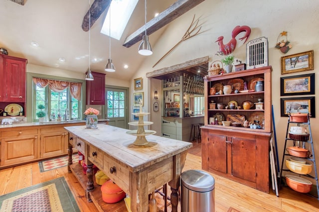 kitchen with a kitchen island, vaulted ceiling with skylight, light countertops, decorative light fixtures, and light wood-type flooring