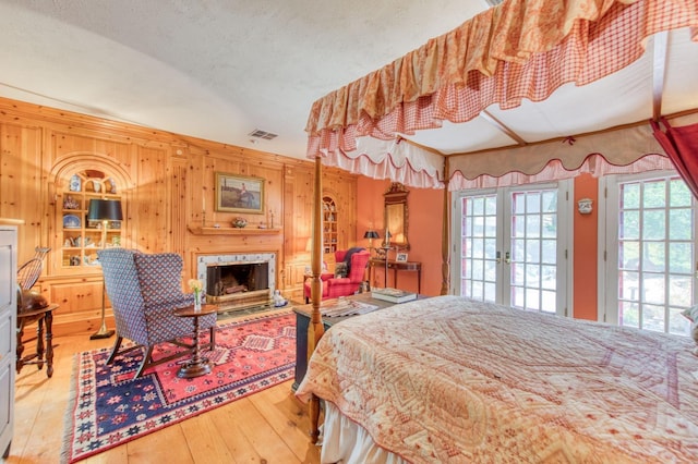 bedroom featuring french doors, wooden walls, a fireplace, and hardwood / wood-style flooring