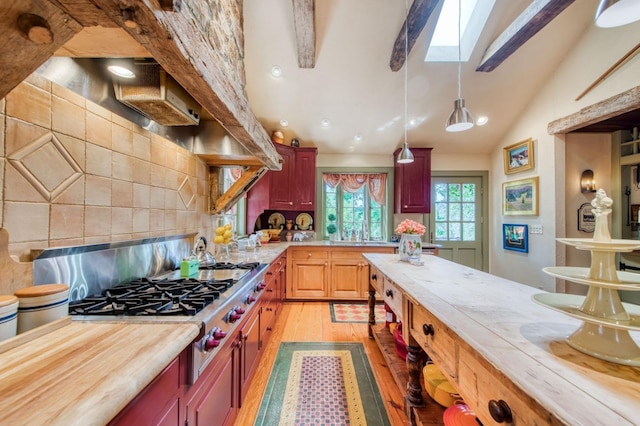 kitchen featuring pendant lighting, vaulted ceiling with skylight, light wood-style floors, decorative backsplash, and stainless steel gas cooktop