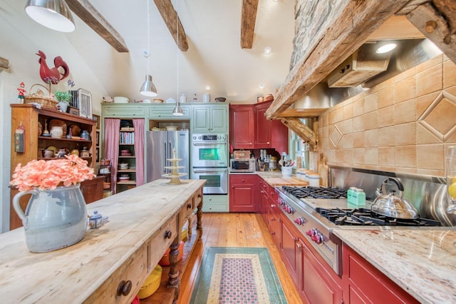 kitchen featuring light wood finished floors, lofted ceiling with beams, appliances with stainless steel finishes, decorative light fixtures, and tasteful backsplash