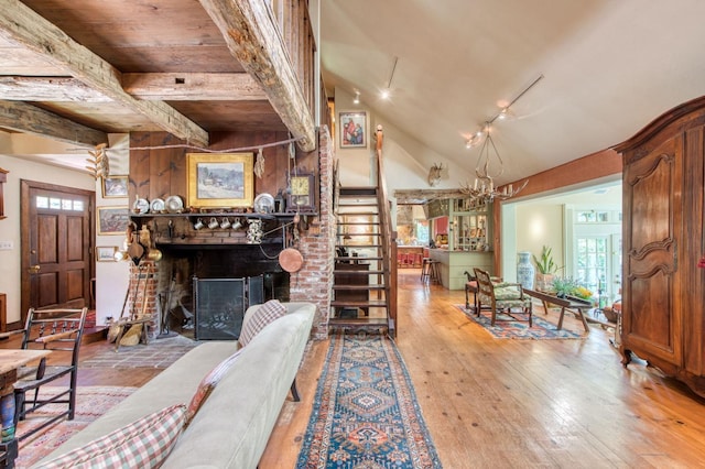 living area featuring a fireplace, hardwood / wood-style flooring, track lighting, vaulted ceiling, and a notable chandelier