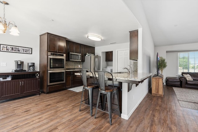 kitchen featuring a breakfast bar area, kitchen peninsula, stainless steel appliances, wood-type flooring, and light stone counters