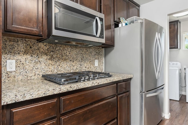 kitchen featuring tasteful backsplash, appliances with stainless steel finishes, washing machine and clothes dryer, dark brown cabinetry, and dark hardwood / wood-style floors