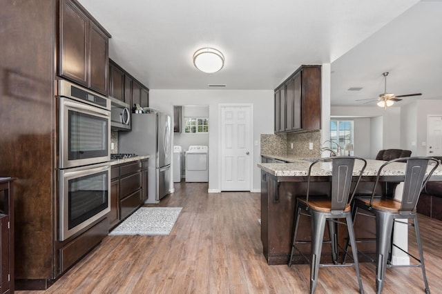 kitchen featuring decorative backsplash, hardwood / wood-style flooring, a breakfast bar area, stainless steel appliances, and washing machine and dryer