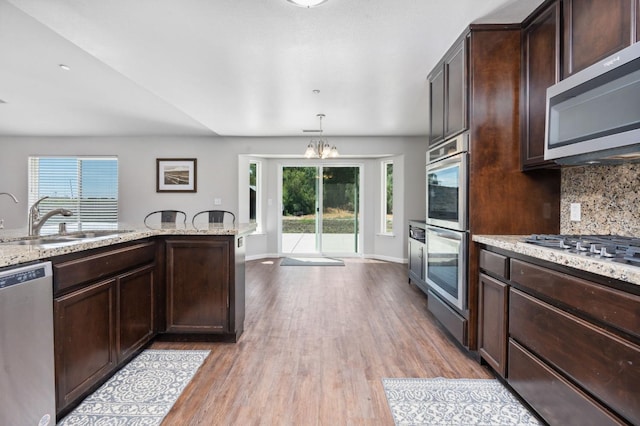 kitchen with stainless steel appliances, light stone countertops, a notable chandelier, pendant lighting, and light wood-type flooring