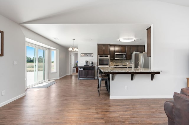 kitchen featuring appliances with stainless steel finishes, dark hardwood / wood-style flooring, lofted ceiling, and a breakfast bar area