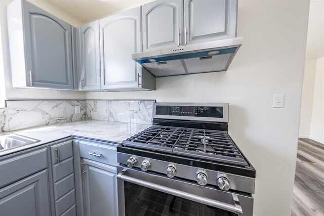 1845 N 10th Ave, Hanford, CA 93230 - kitchen featuring stainless steel gas stove, under cabinet range hood, wood finished floors, decorative backsplash, and gray cabinets