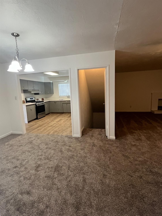 kitchen with light carpet, a textured ceiling, gray cabinetry, stainless steel range, and a notable chandelier