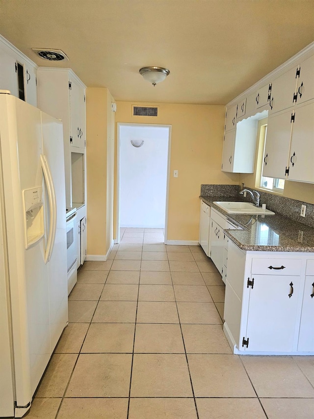 kitchen with dark stone counters, white appliances, sink, light tile patterned floors, and white cabinetry