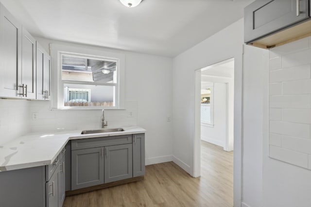 kitchen with light wood-type flooring, a wealth of natural light, sink, and light stone countertops