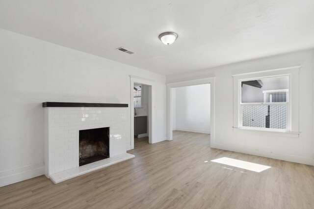 unfurnished living room featuring light hardwood / wood-style floors and a brick fireplace