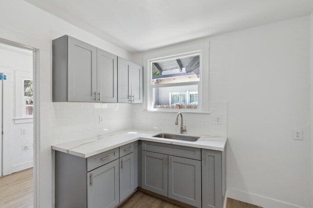 kitchen with sink, decorative backsplash, gray cabinetry, and wood-type flooring