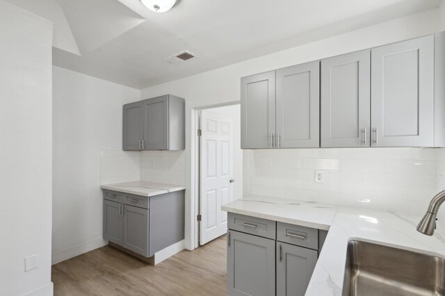 kitchen with light wood-type flooring, backsplash, gray cabinetry, light stone counters, and sink