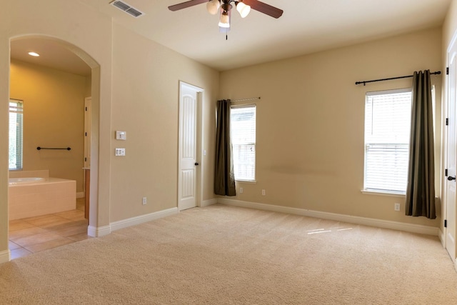 unfurnished bedroom featuring ceiling fan, light carpet, ensuite bathroom, and multiple windows