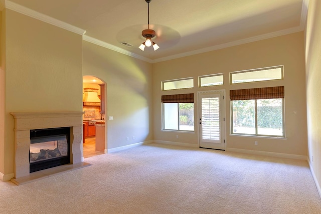 unfurnished living room featuring ceiling fan, a multi sided fireplace, ornamental molding, and light carpet