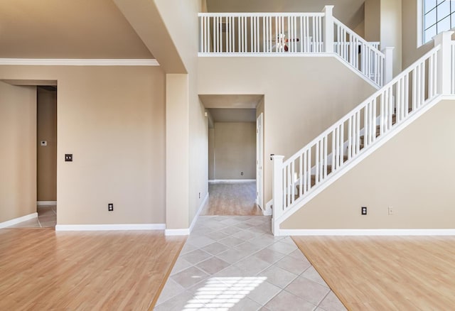 entrance foyer with crown molding, a high ceiling, wood finished floors, baseboards, and stairs