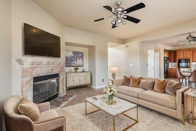 living room with a ceiling fan, a high end fireplace, baseboards, and wood finished floors