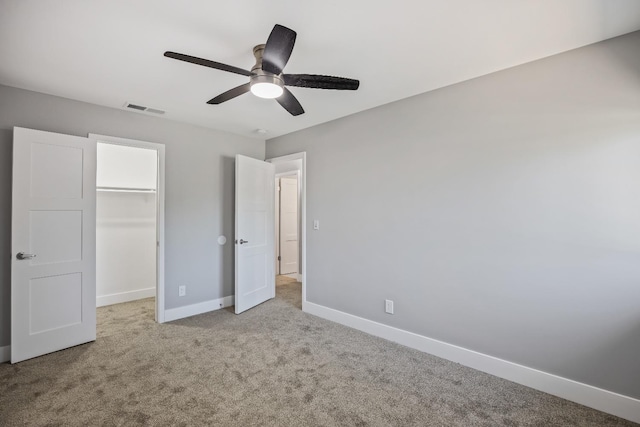 unfurnished bedroom featuring ceiling fan, a closet, light colored carpet, and a walk in closet