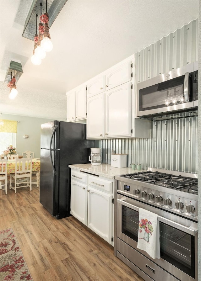 kitchen featuring stainless steel appliances, light wood-type flooring, white cabinets, and a textured ceiling