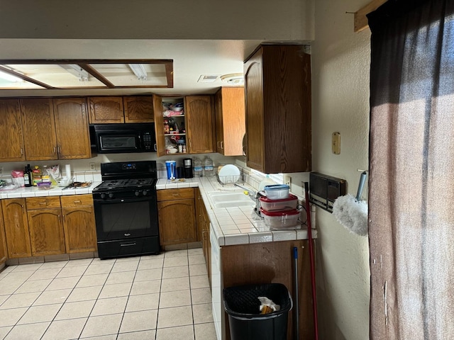 kitchen with light tile patterned floors, sink, tile counters, and black appliances