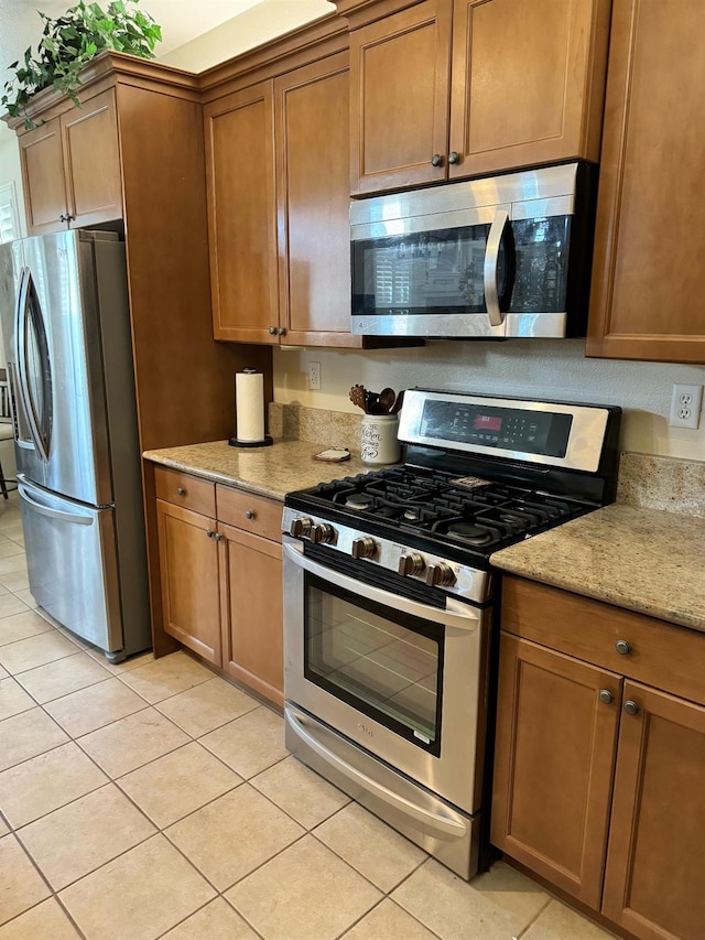 kitchen featuring light tile patterned flooring, appliances with stainless steel finishes, and light stone countertops