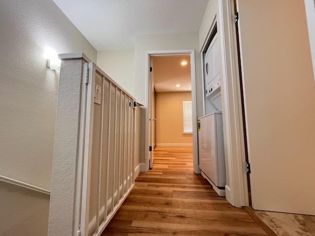 hallway featuring light wood finished floors, stacked washer and clothes dryer, and baseboards