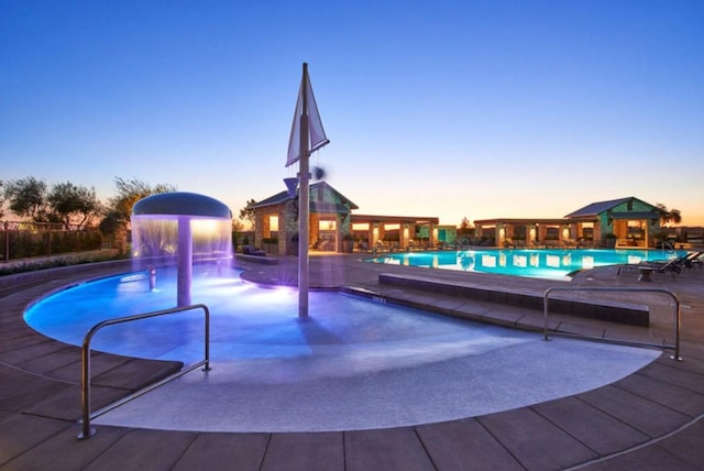 pool at dusk with a patio area and pool water feature