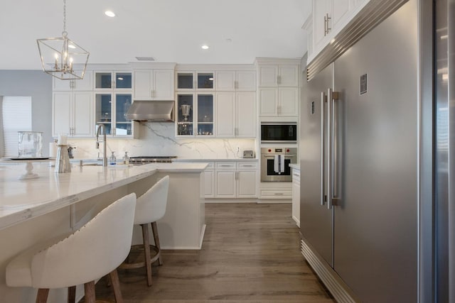 kitchen featuring backsplash, white cabinetry, sink, wood-type flooring, and built in appliances