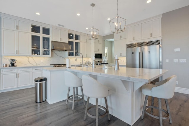 kitchen with built in appliances, dark hardwood / wood-style flooring, an island with sink, and white cabinetry