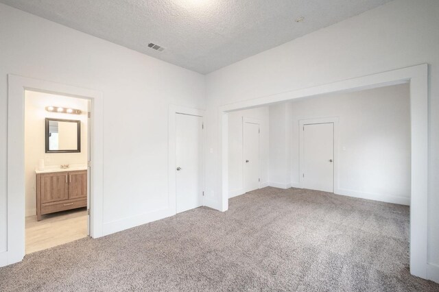 unfurnished bedroom featuring sink, ensuite bath, a closet, a textured ceiling, and light carpet