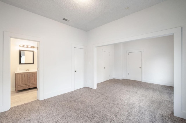 unfurnished bedroom featuring light carpet, a sink, visible vents, and a textured ceiling