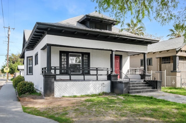 view of front facade featuring covered porch, roof with shingles, and stucco siding