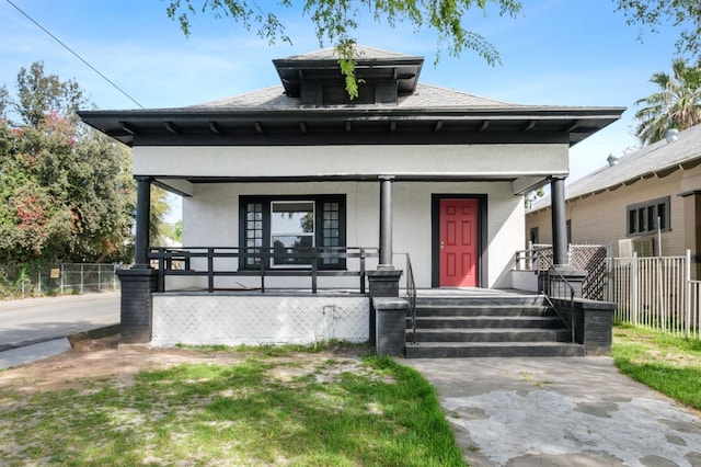 view of front facade with a shingled roof, fence, a porch, and stucco siding