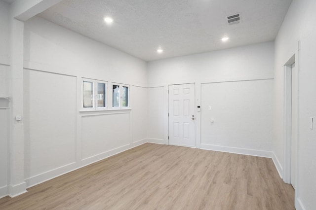 empty room with light wood finished floors, recessed lighting, visible vents, a textured ceiling, and baseboards