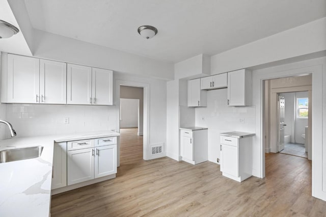 kitchen with decorative backsplash, sink, white cabinets, and light wood-type flooring